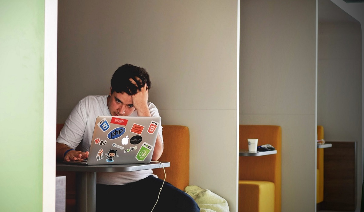 Male visually stressed while working on a laptop in a community workspace